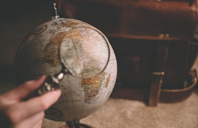 person holding magnifying glass near desk globe